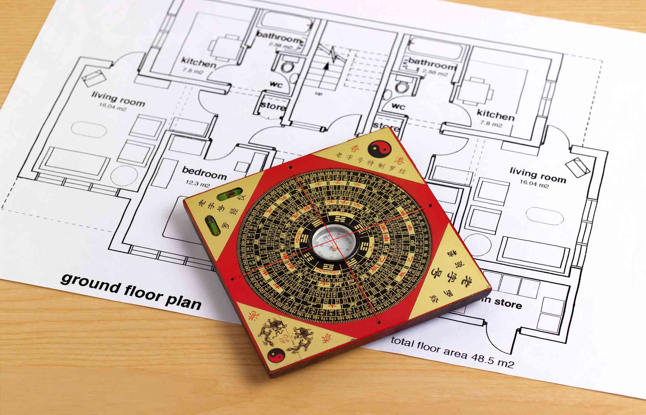 A Chinese feng shui compass with intricate markings rests on an architectural floor plan. The layout includes labeled rooms. The scene conveys balance.